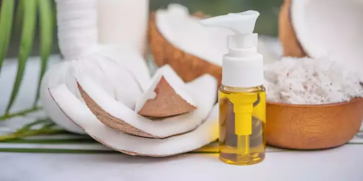 Pedaços de coco empilhados em uma mesa  juntamente com um spray contendo óleo de coco