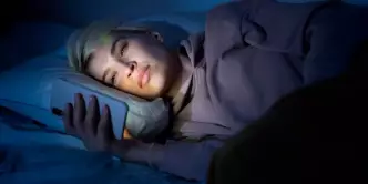 Pessoa com isônia mexendo no celular na cama em um quarto escuro