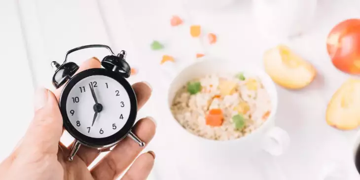 Um mesa com café da manhã e uma mão segurando um relógio simbolizando o jejum intermitente