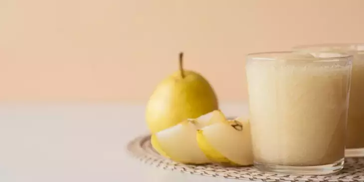 Um copo de suco de pera com peras ao lado pronto para ser consumido para aliviar a azia