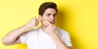 Jovem espremendo uma espinha ao fundo de uma parede amarela