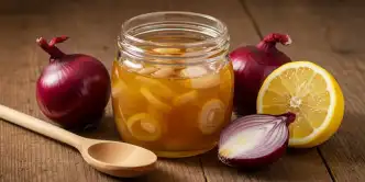 Mesa com colher de pau cebolas roxas e uma pequena jarra com xarope de cebola e mel