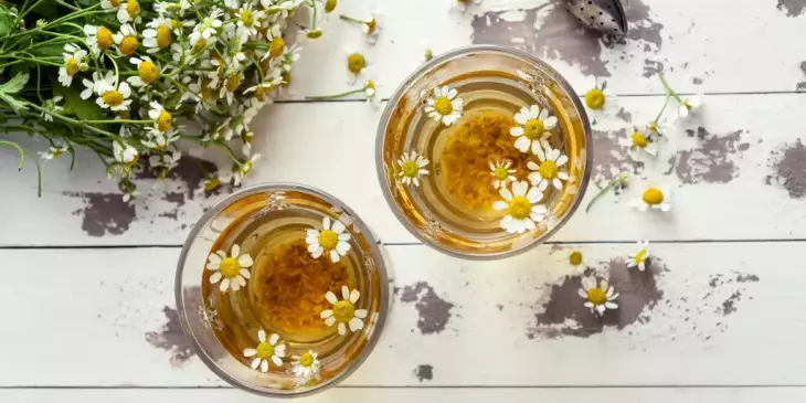 Vista superior de xícaras de chá de camomila usada como calmante natural em uma mesa de madeira pintada de branco